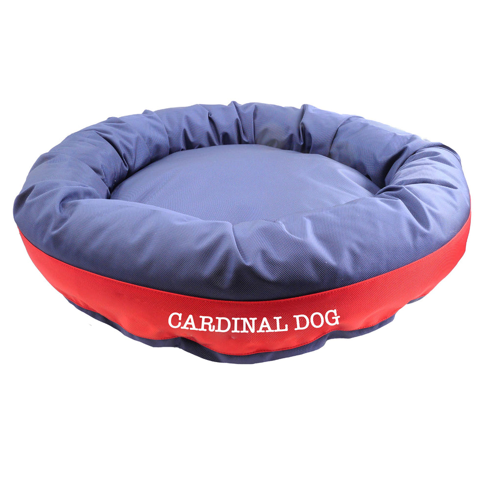 Blue round bolstered dog bed with a red band in the middle with white embroidered 'Carinal Dog'.