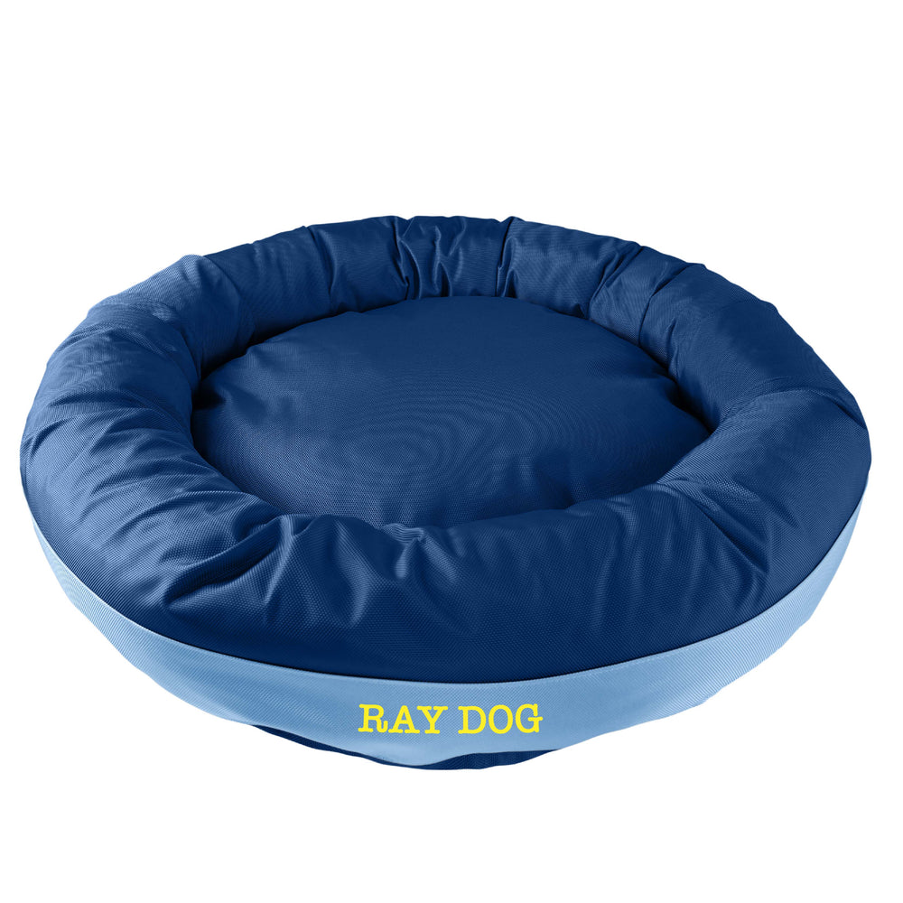 Dark blue round bolstered dog bed with a light blue band and yellow embroidered 'Ray Dog'.