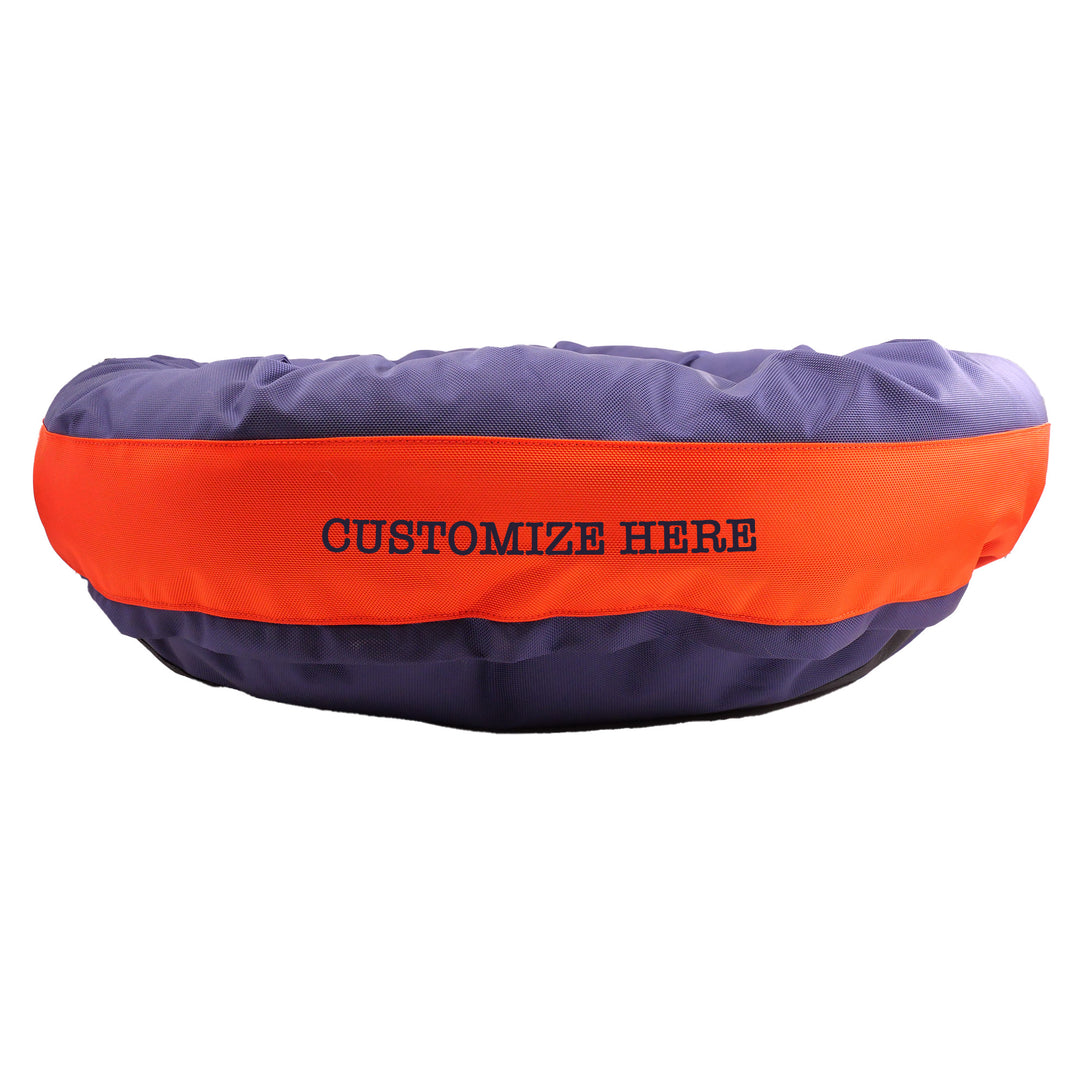 Blue round bolstered dog bed with an orange band with Navy embroidered 'Customize Here'.