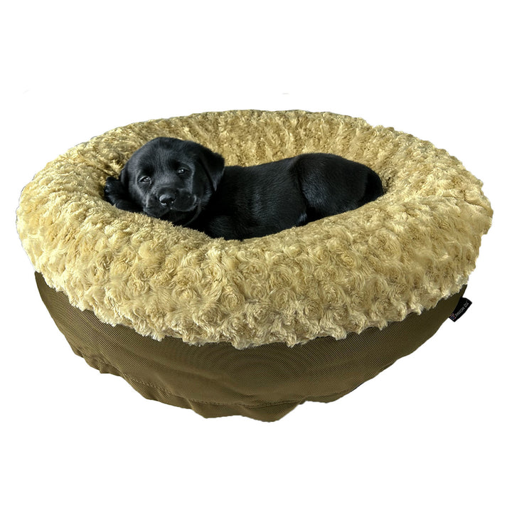 Black puppy lying on a beige fluffy round bolstered dog bed 
