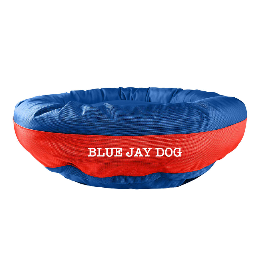 Blue bolstered dog bed with red band in center with 'Blue Jay Dog' white embroidery.