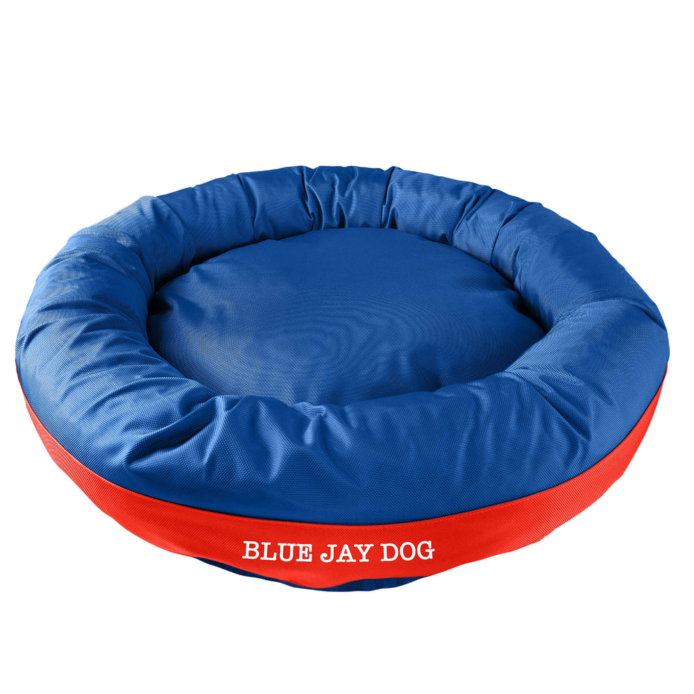 Blue bolstered dog bed with red band in center with 'Blue Jay Dog' white embroidery.
