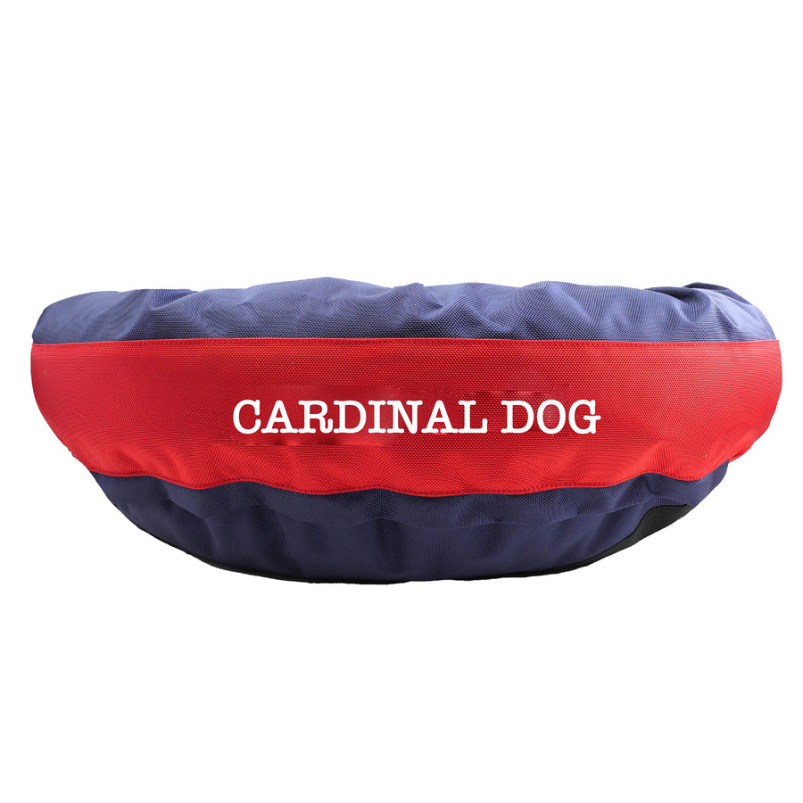 Blue round bolstered dog bed with a red band in the middle with white embroidered 'Carinal Dog'.