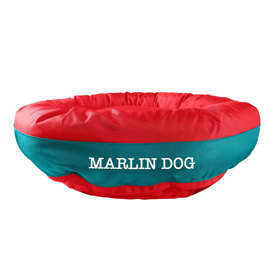 Orange round bolstered dog bed with a teal band and white embroidered 'Marlin Dog'.