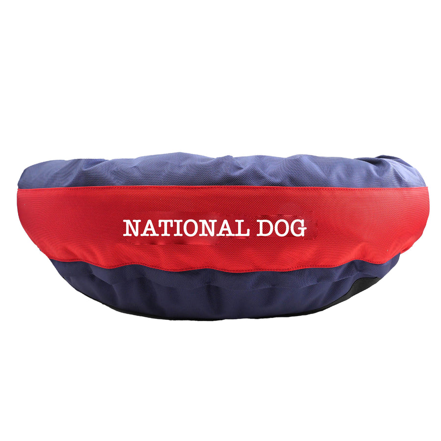 Navy round bolstered dog bed with red band and white embroidered 'National Dog'.