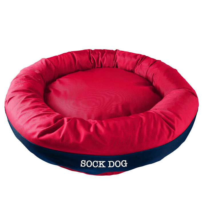 Red round bolstered dog bed with a navy band and white embroidered 'Sock Dog'.