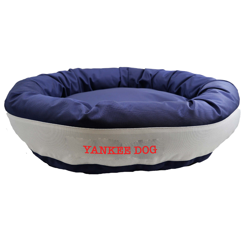 Navy round bolstered dog bed with a silver band and red embroidered 'Yankee Dog'.