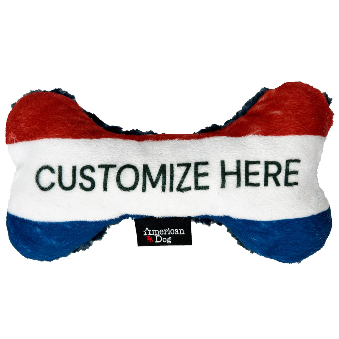 Red, white, and blue  fleece bone-shaped toy with 'Customize Here' text and American Dog brand logo.