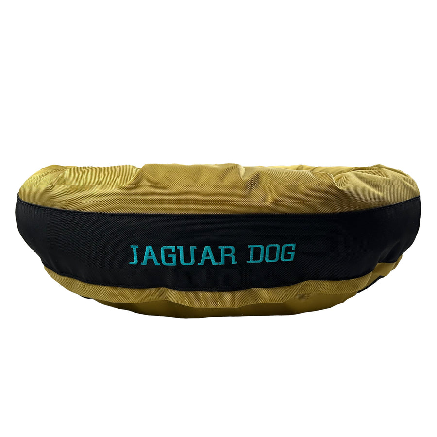 Gold round bolstered dog bed with a black band and teal embroidered 'Jaguar Dog'.
