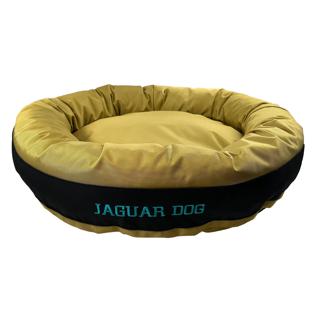Gold round bolstered dog bed with a black band and teal embroidered 'Jaguar Dog'.
